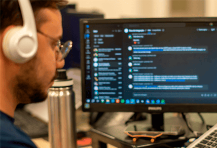 Profissional com fones trabalha em computador com código